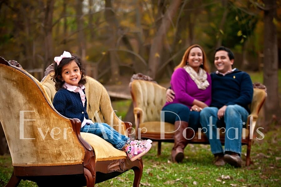 Family sitting on gold sofas in outdoor portrait.